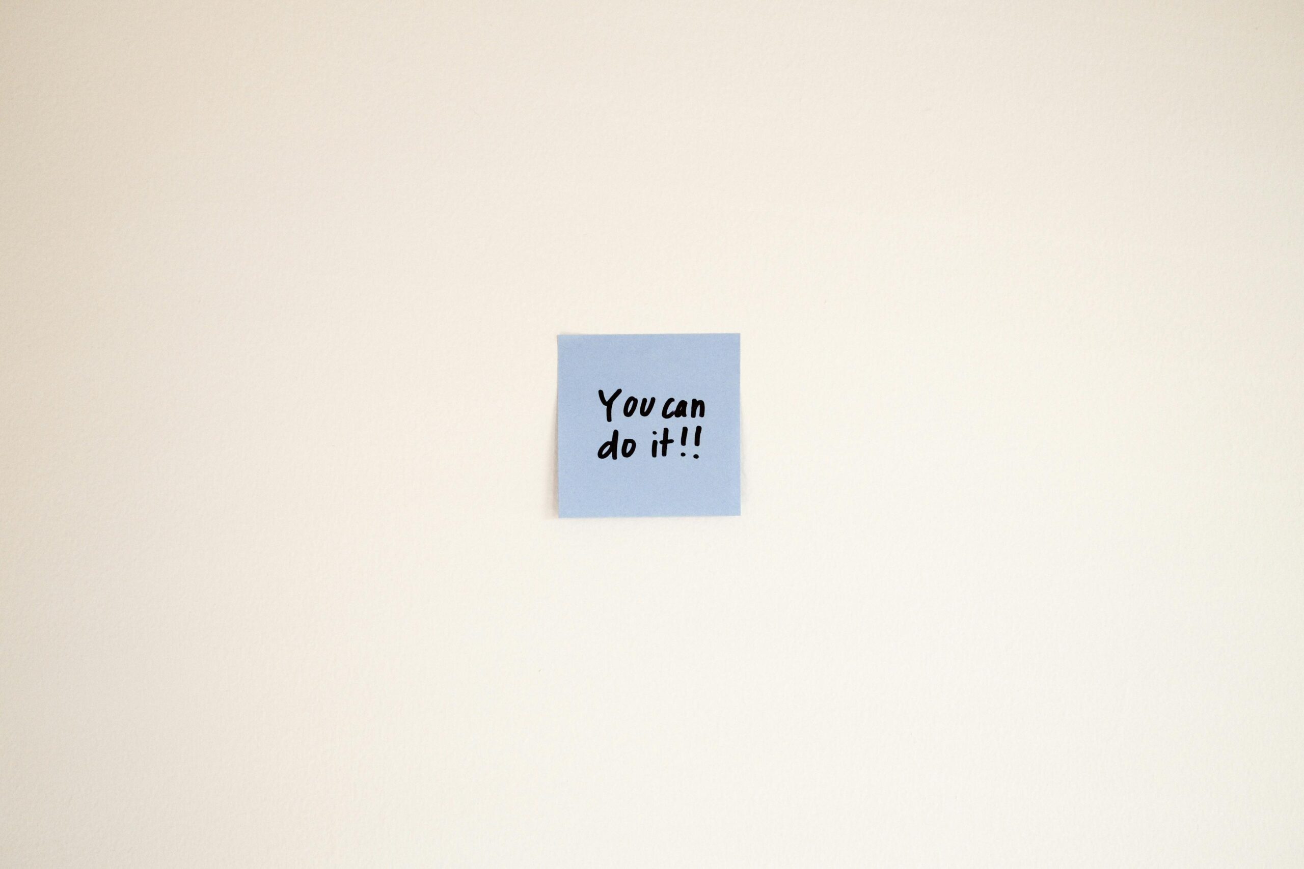 pexels-photo-29546585-29546585-1 A motivational message on a blue Post-it note reads 'You can do it!' on a cream wall.